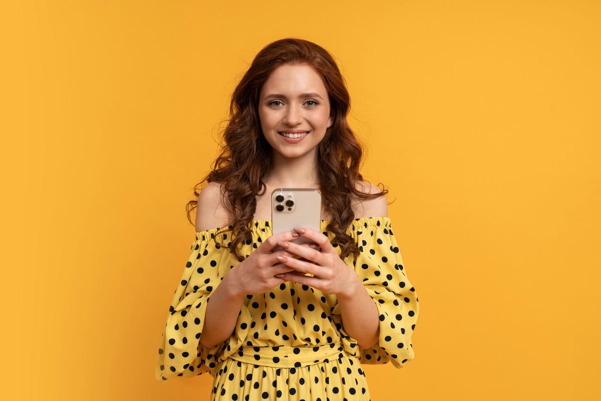 girl taking a selfie in a yellow dress and vibrant orange background